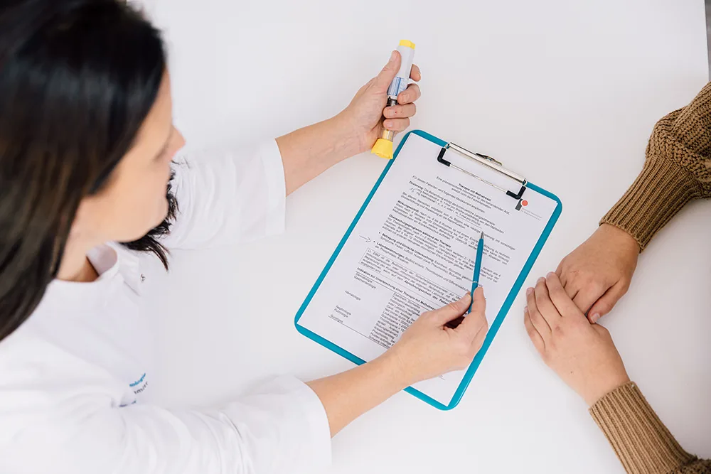 Ärztin erläutert einer Patientin einen Befund auf dem Klemmbrett